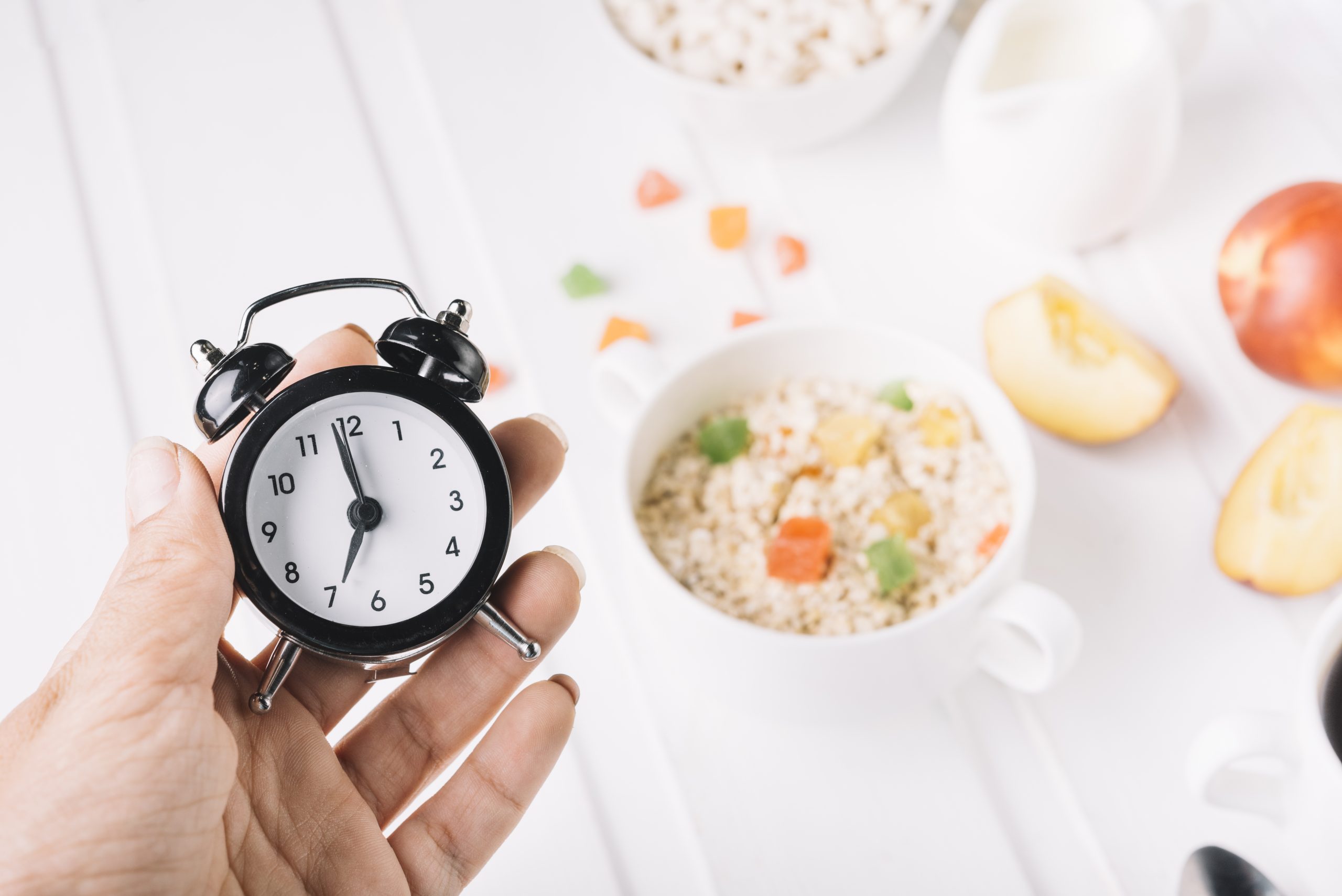person-s-hand-holding-alarm-clock-hand-breakfast-table