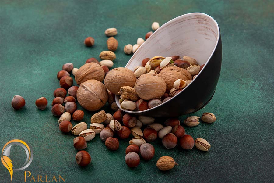 side view mix nuts walnuts pistachios hazelnuts peanuts bowl green surface